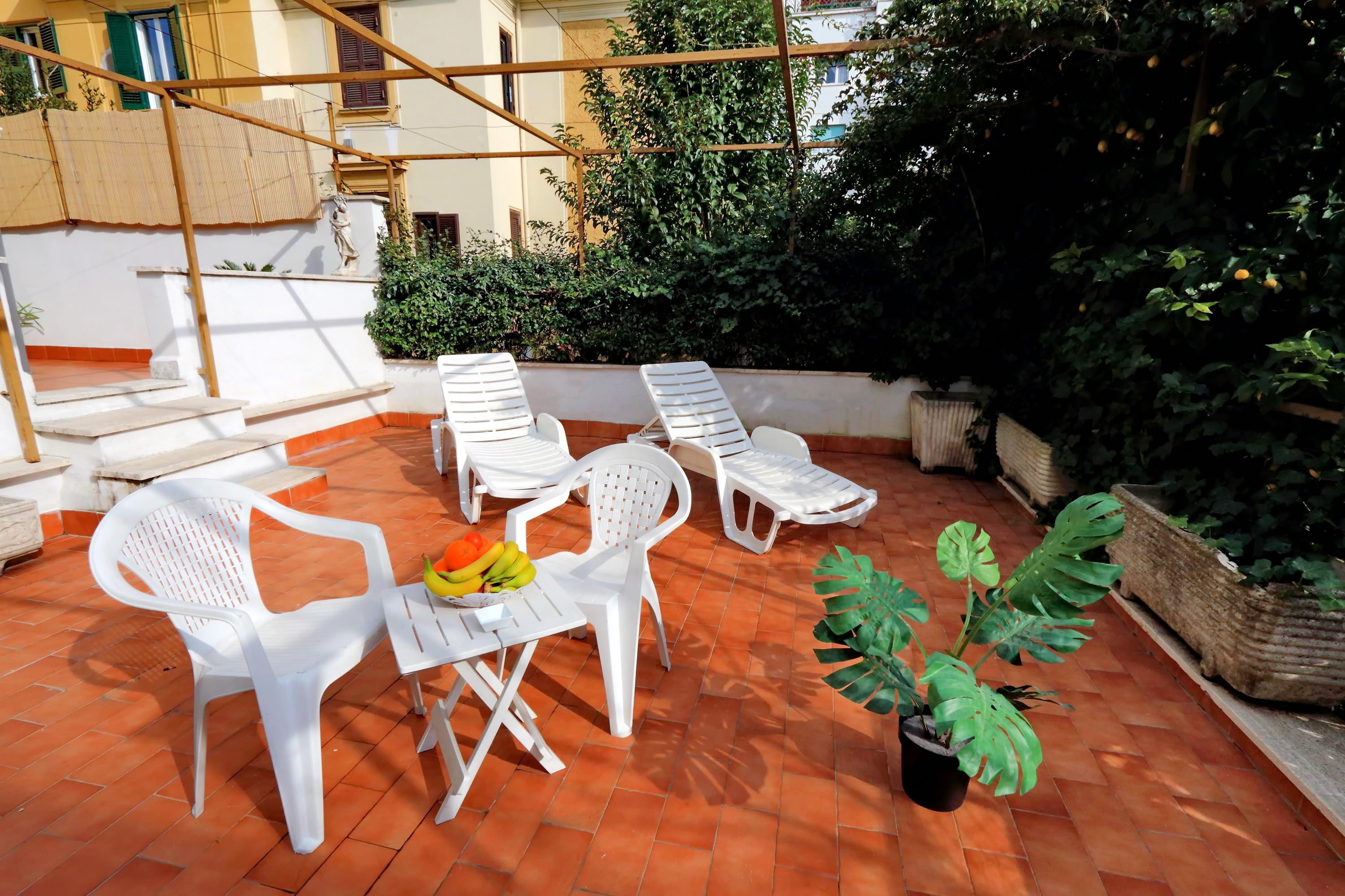 Une terrasse sur le toit avec des chaises en plastique blanches, une petite table sur laquelle on a posé des fruits et une plante en pot.