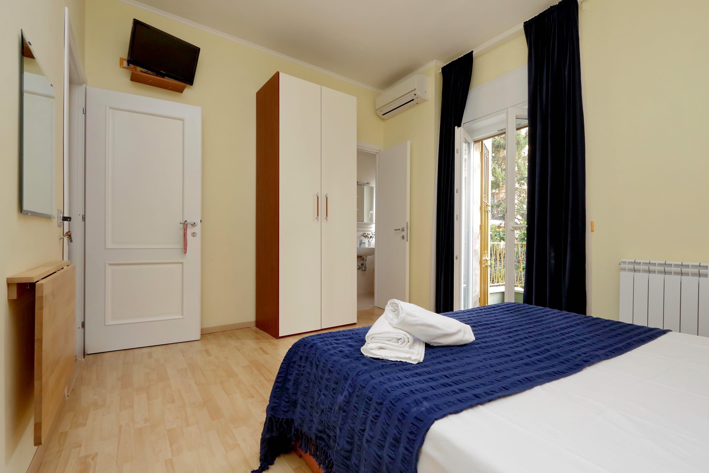 Ein Schlafzimmer mit einem Bett, einem Kleiderschrank, einem Fernseher und einem Fenster mit Vorhängen.