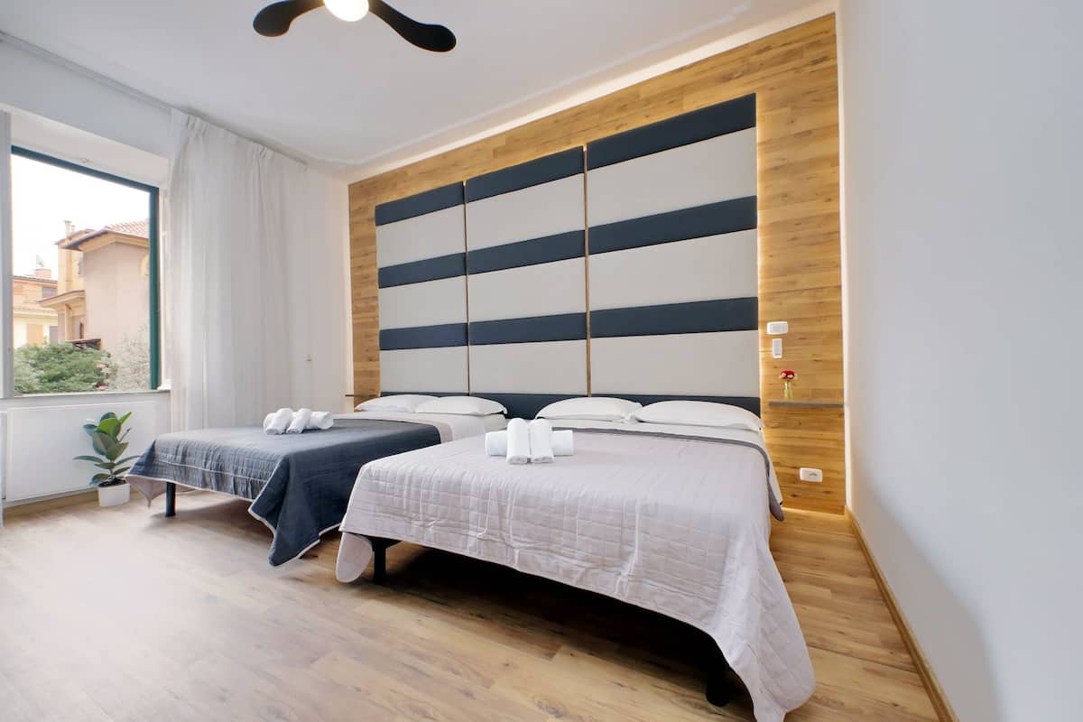 A hotel room with two beds, a wooden accent wall, a potted plant, and a window with a view.