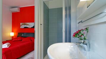 Ein Hotelzimmer mit einem roten Bett, einem weißen Waschbecken mit Spiegel und einer Duschkabine.