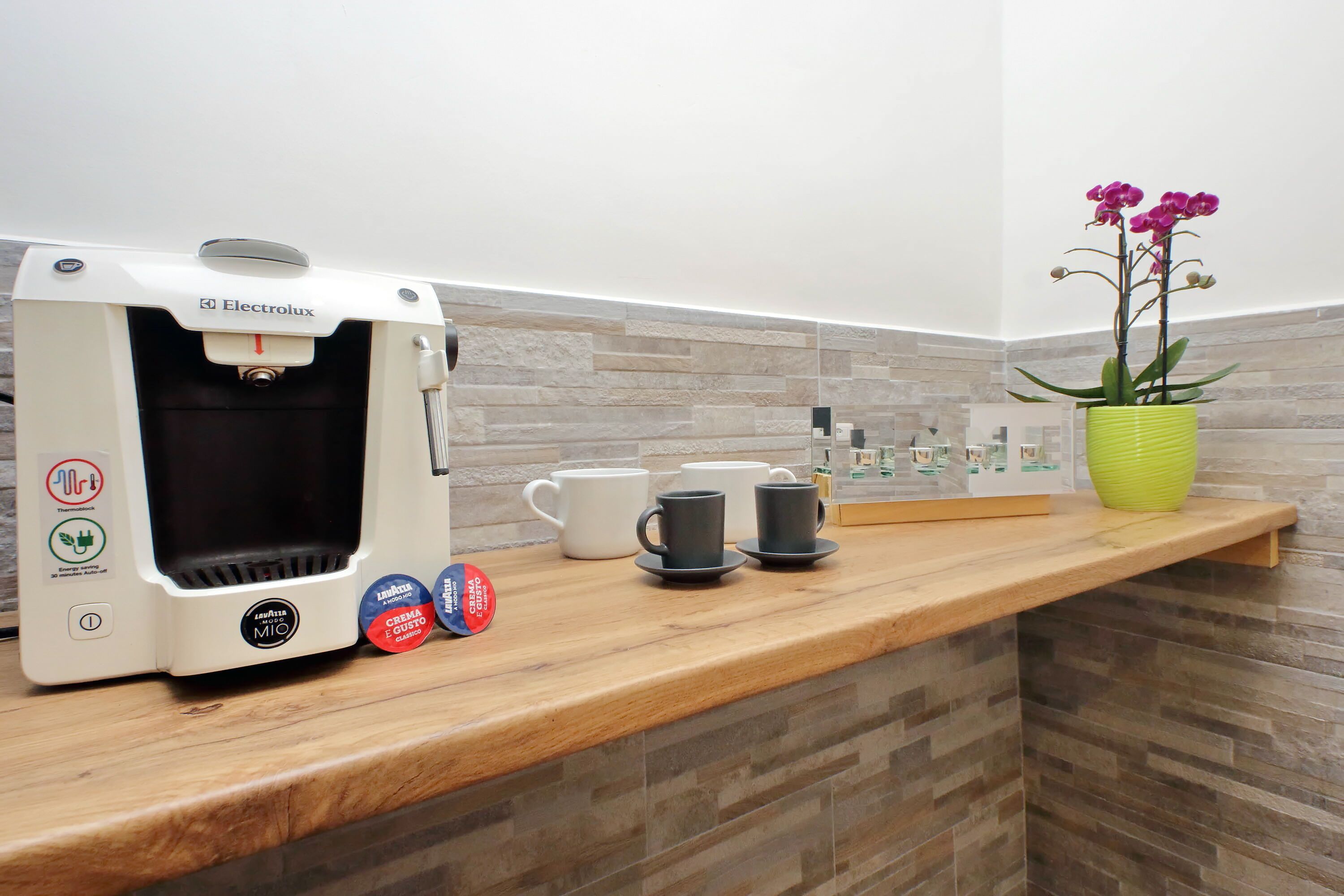 A coffee machine, cups, and a potted orchid on a counter.