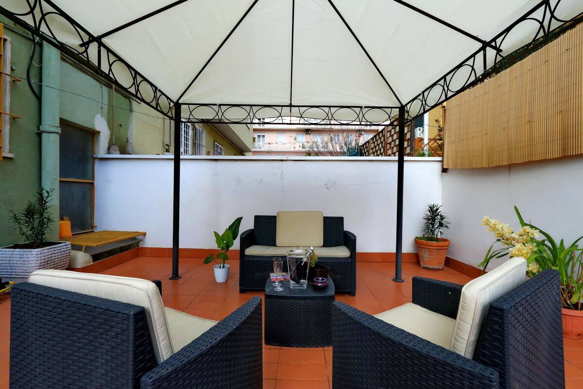 An outdoor patio with wicker furniture, a table with drinks, and potted plants.