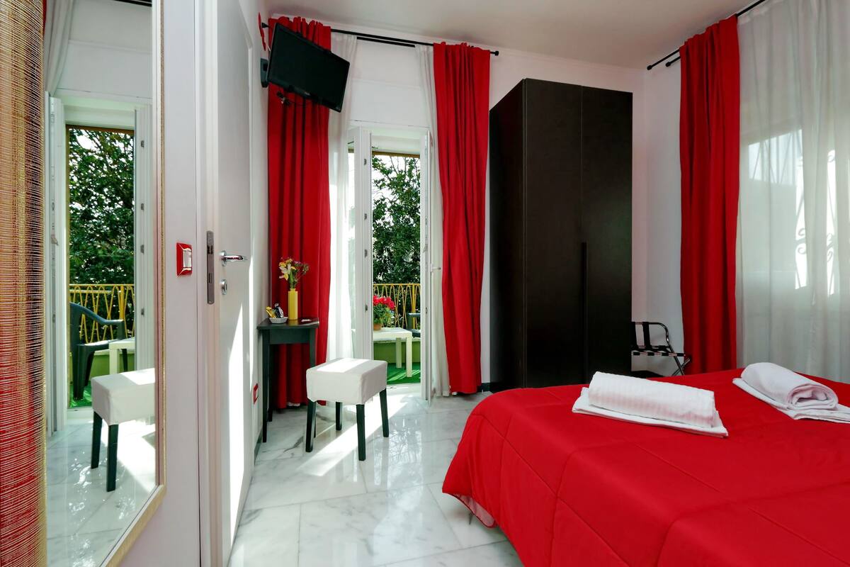 A hotel room with a bed, a desk, and a chair. There is a door leading to an outdoor area with a table and chairs.