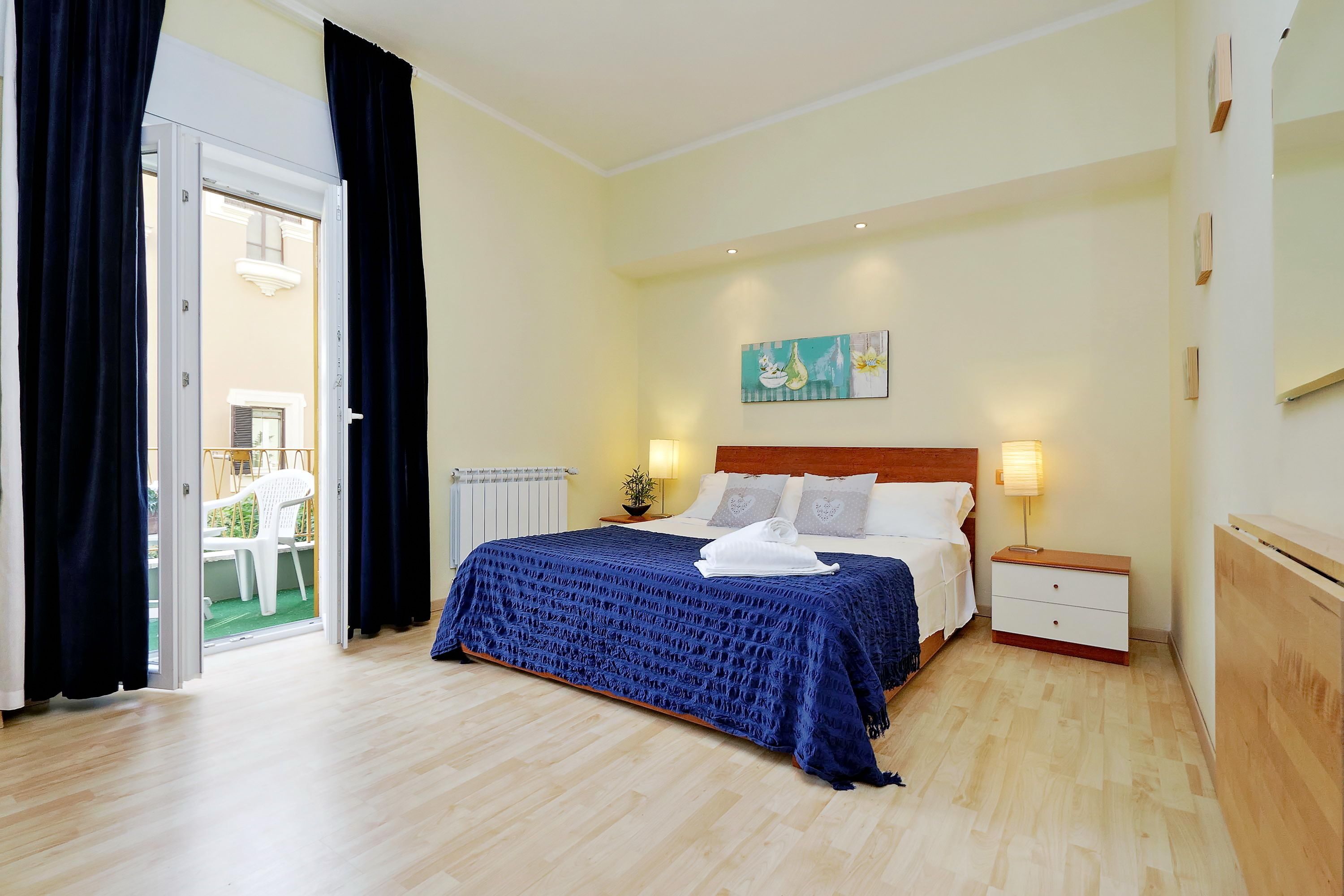 A bedroom with a bed, bedside tables, a painting, and a view through an open door.