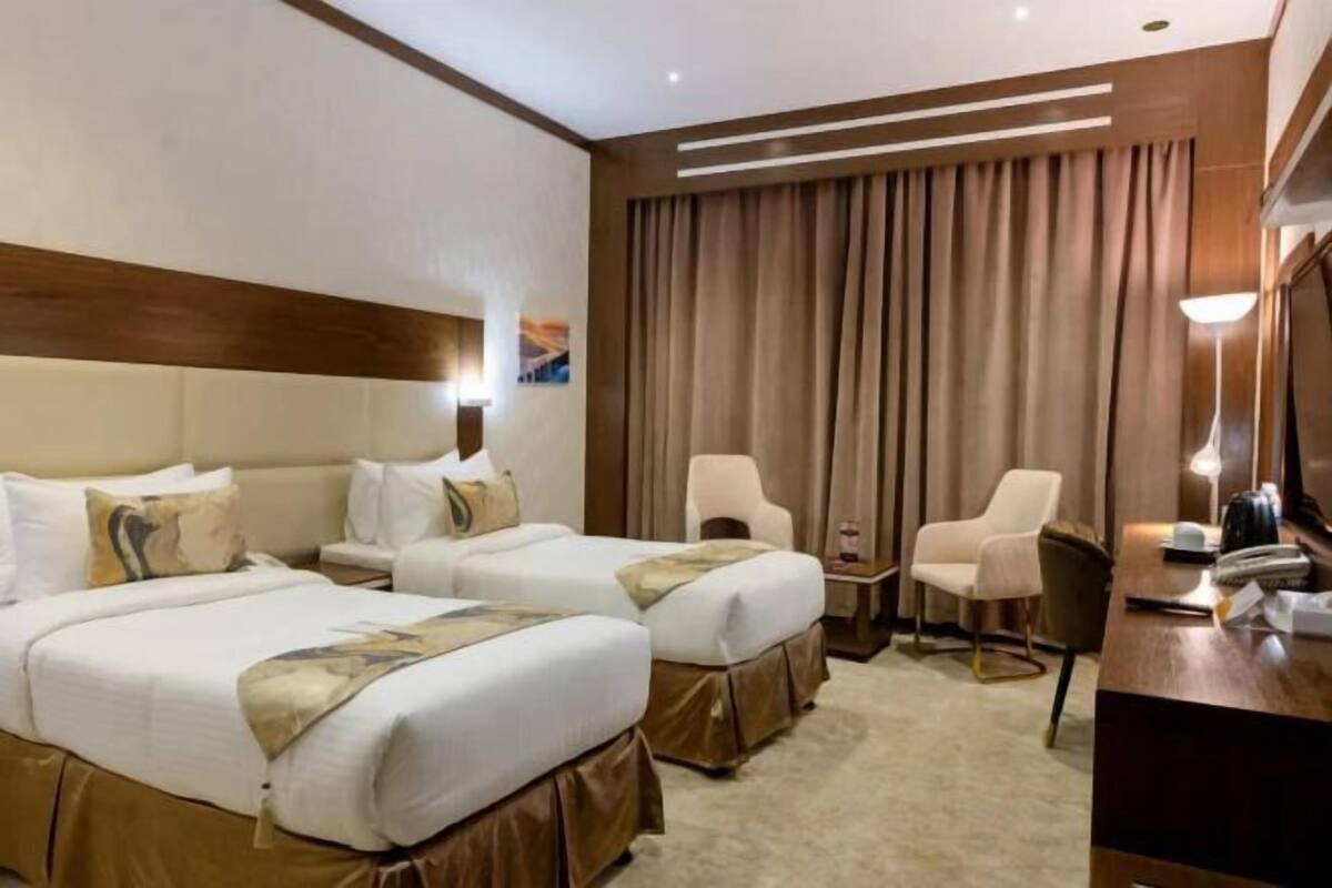 A hotel room with two beds, a desk, a chair, and a television.