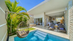 Uma área de piscina moderna ao ar livre, com uma cadeira suspensa, espreguiçadeiras e uma parede de pedra.