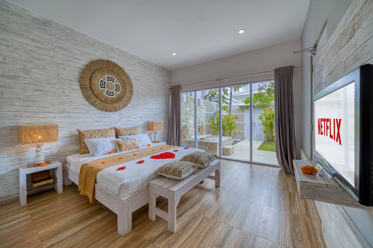 A modern bedroom with a large bed, a bench, a TV, and a view of the outdoors.