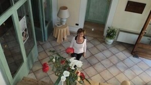 Una mujer caminando en una habitación con piso de baldosas, un sofá, una lámpara y una planta en maceta.