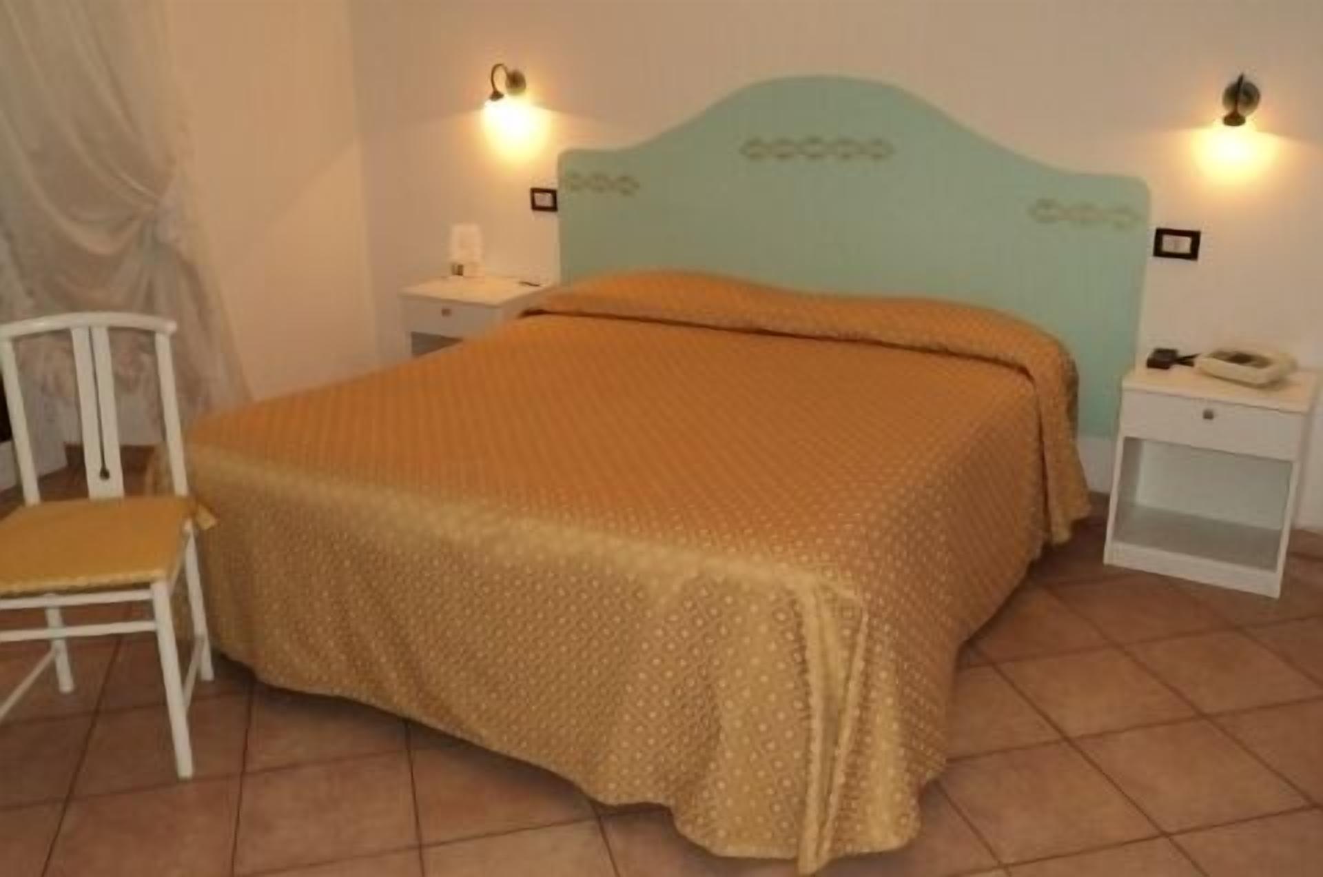 A bedroom with a bed, a chair, two bedside tables, and wall-mounted lights.