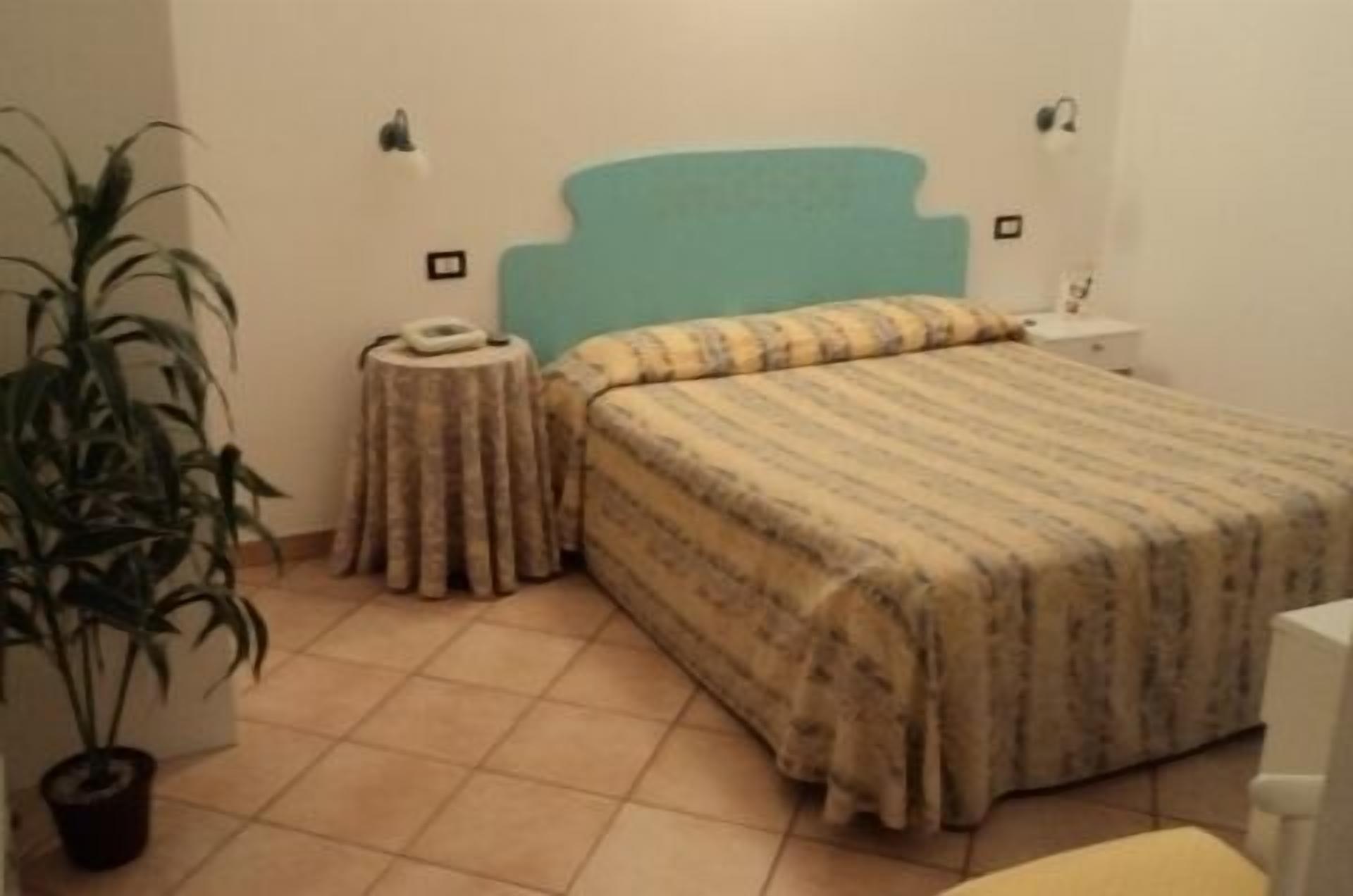 A bedroom with a bed, a bedside table, a lamp, and a potted plant.