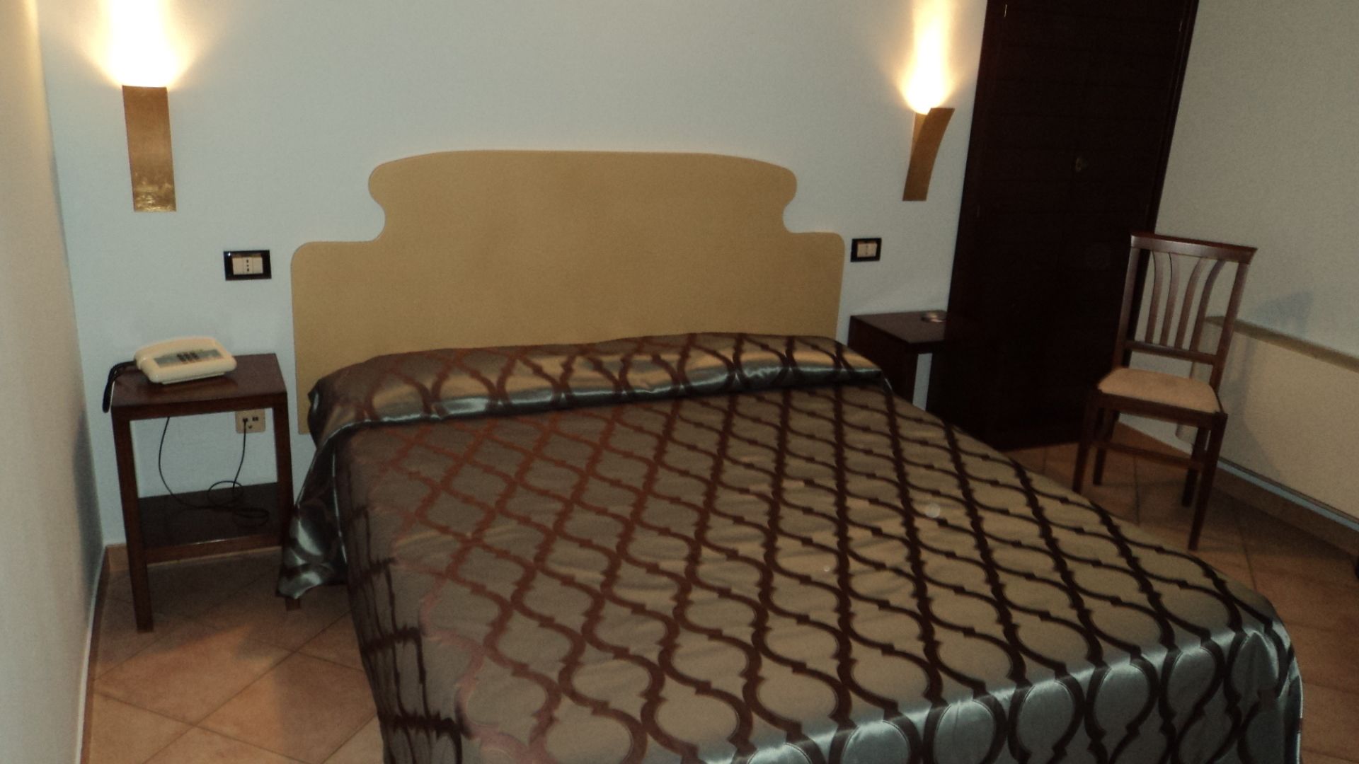 A bedroom with a bed, bedside tables, a chair, and wall-mounted lights.