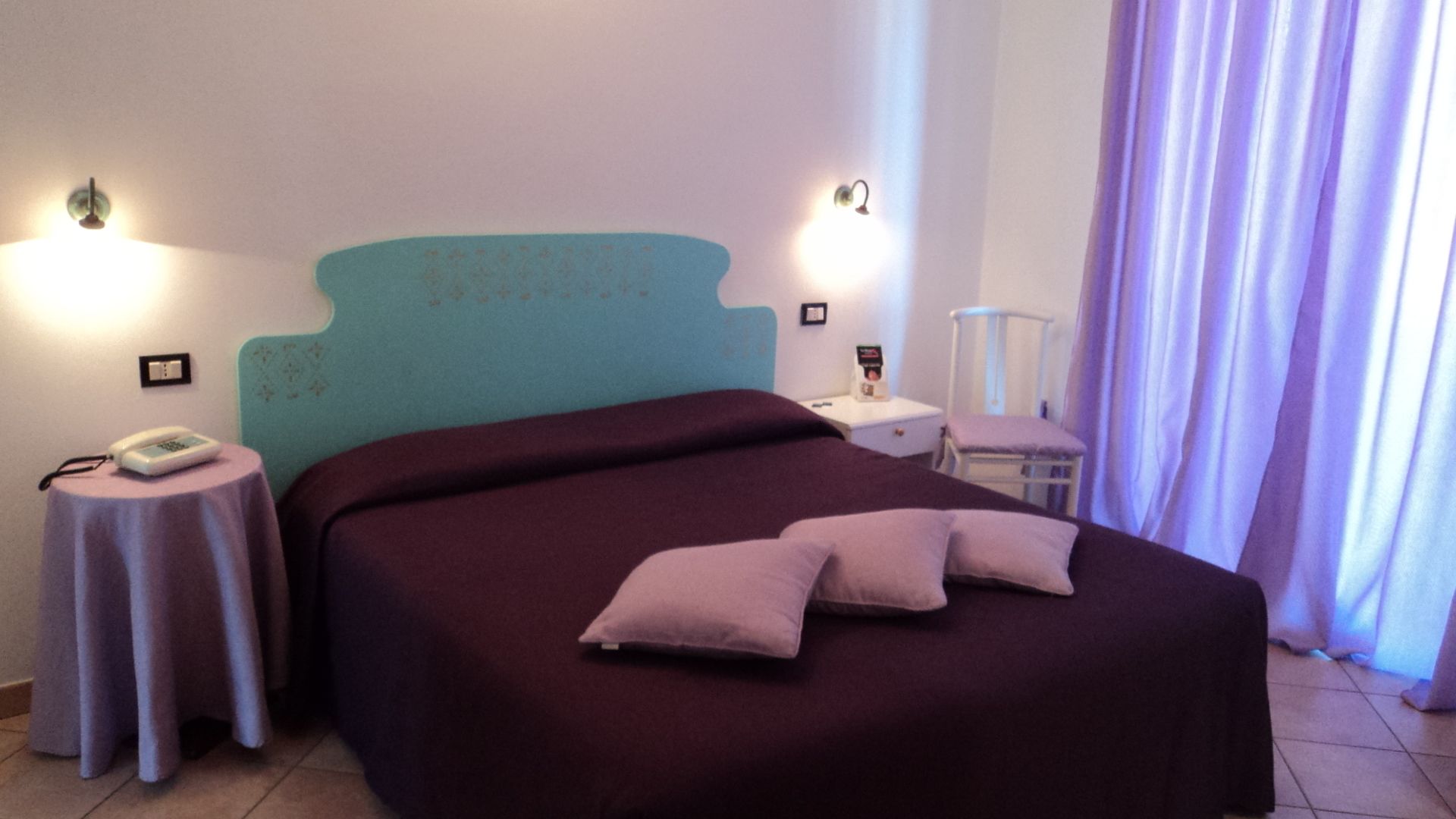 A bedroom with a bed, a nightstand, a chair, and a wall-mounted lamp.