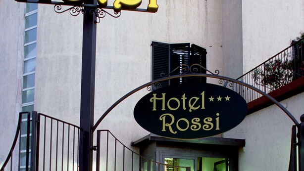 Entrada de un hotel con un letrero que dice "Hotel Rossi" y una puerta con rejas.