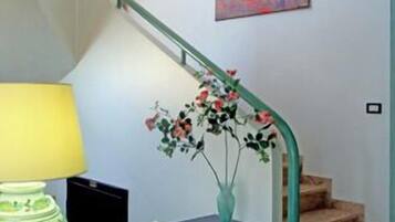 Un escalier avec une rampe verte, un tableau accroché au mur, un vase rempli de fleurs et une table sur laquelle se trouvent une lampe et un bol décoratif.