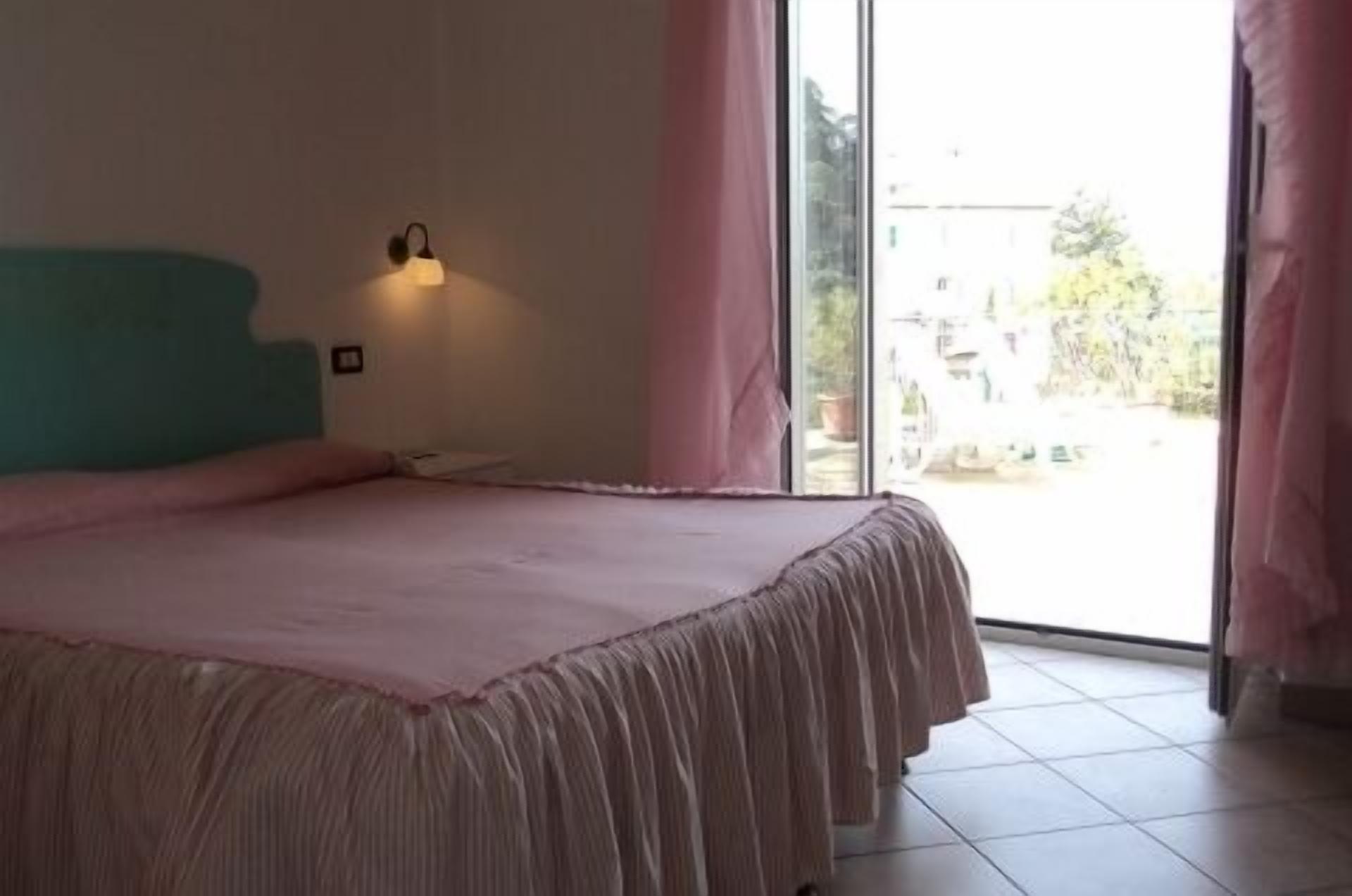 Une chambre à coucher comprenant un lit, une table de chevet, une lampe fixée au mur et une vue sur l’extérieur grâce  à une grande fenêtre.