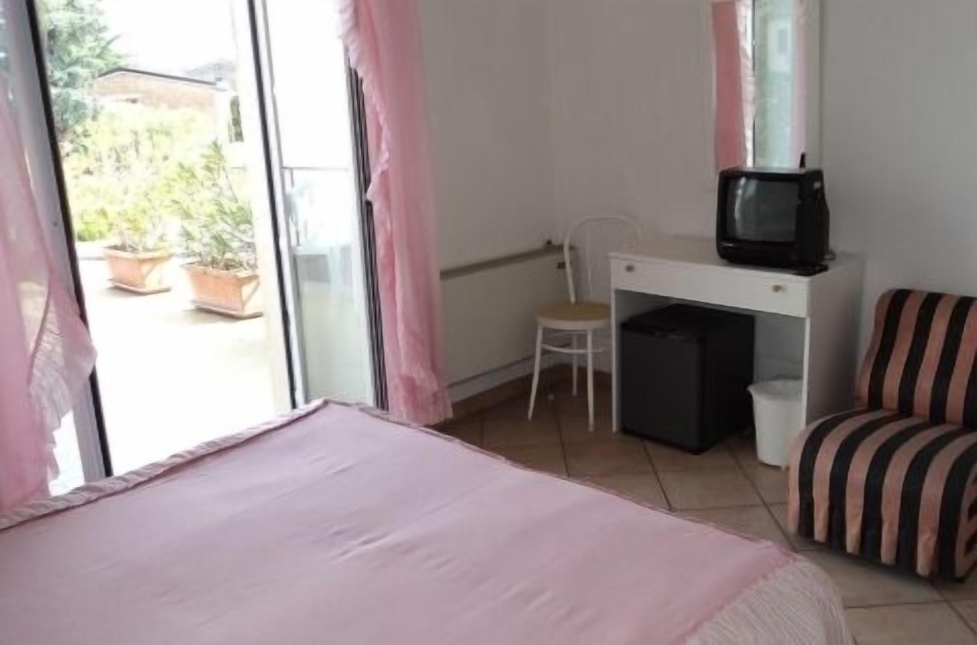 Un dormitorio con una cama, un escritorio con una silla, un televisor y una silla a rayas.