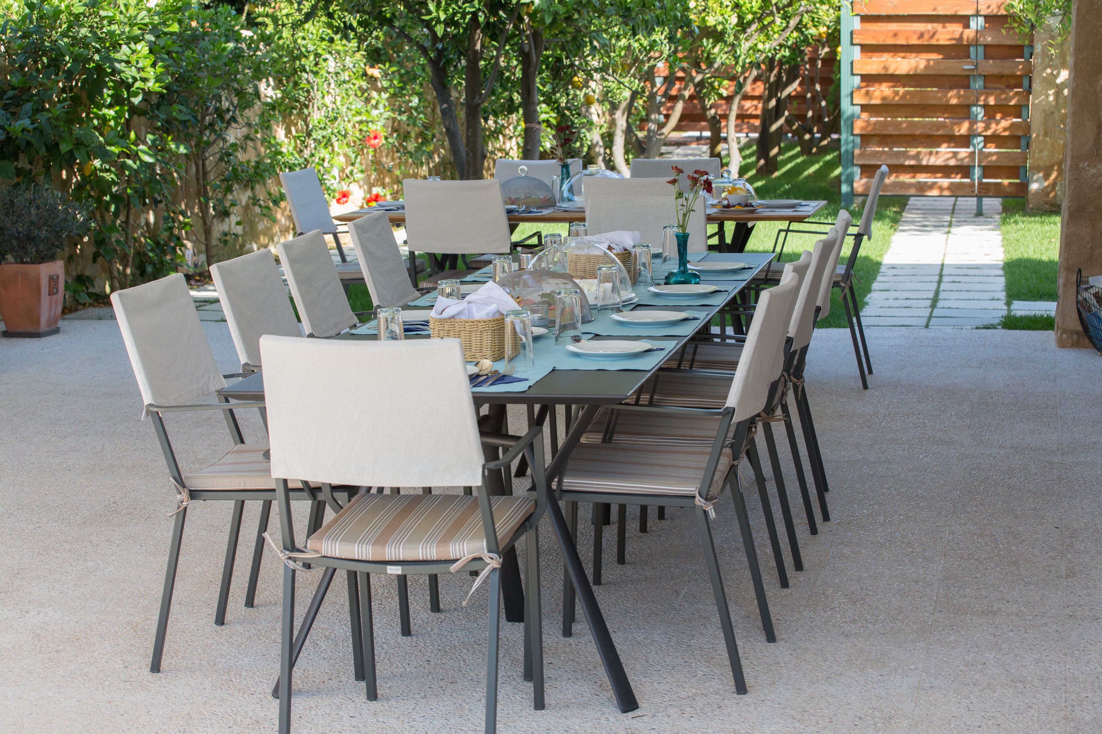 An outdoor dining area with a long table set for multiple people, surrounded by chairs.