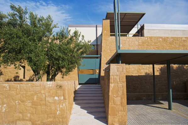 A modern building with a stone facade, a covered outdoor area, and a staircase leading to a higher level.