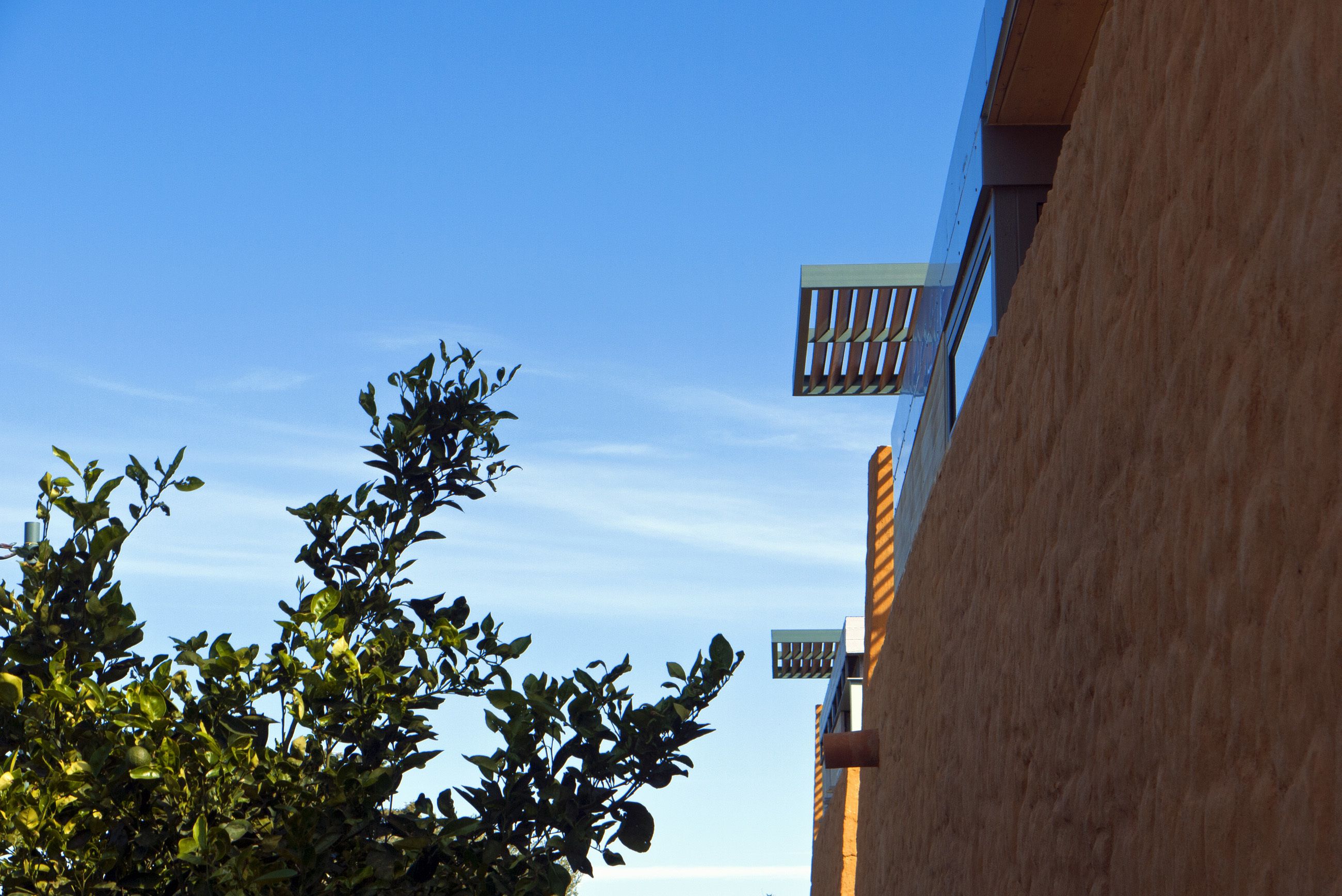 Een gebouw met blauwe lucht, een balkon en een boom met groene bladeren.