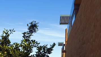 Een gebouw met blauwe lucht, een balkon en een boom met groene bladeren.
