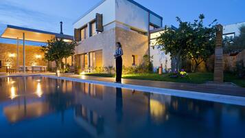 A modern house with a swimming pool, stone facade, and outdoor lighting.