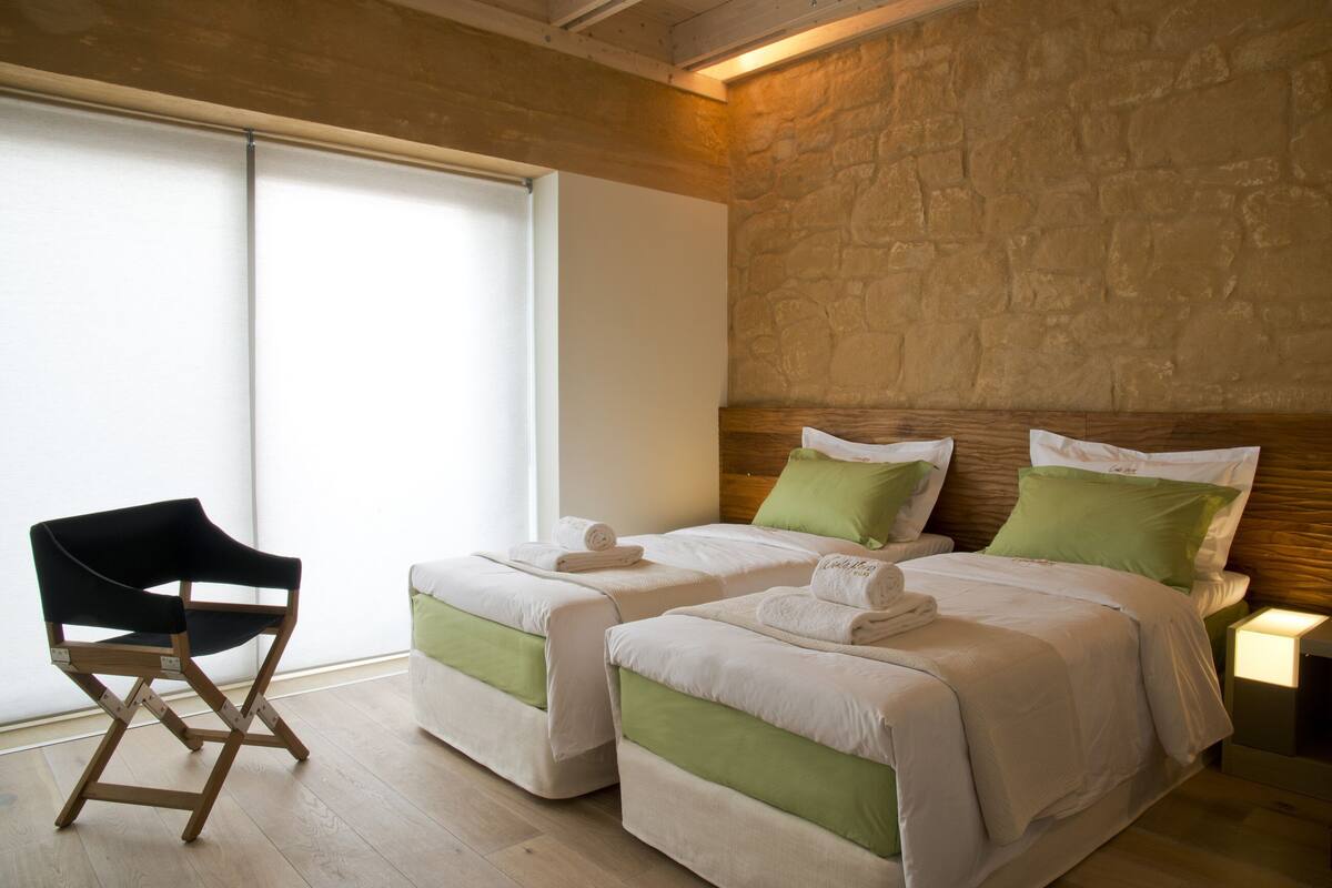A hotel room with two beds, a wooden chair, and a stone wall.