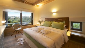 A modern bedroom with a large bed, a desk, and a chair. There are windows offering a view of the city. - Conte Marino Villas (Platanias)