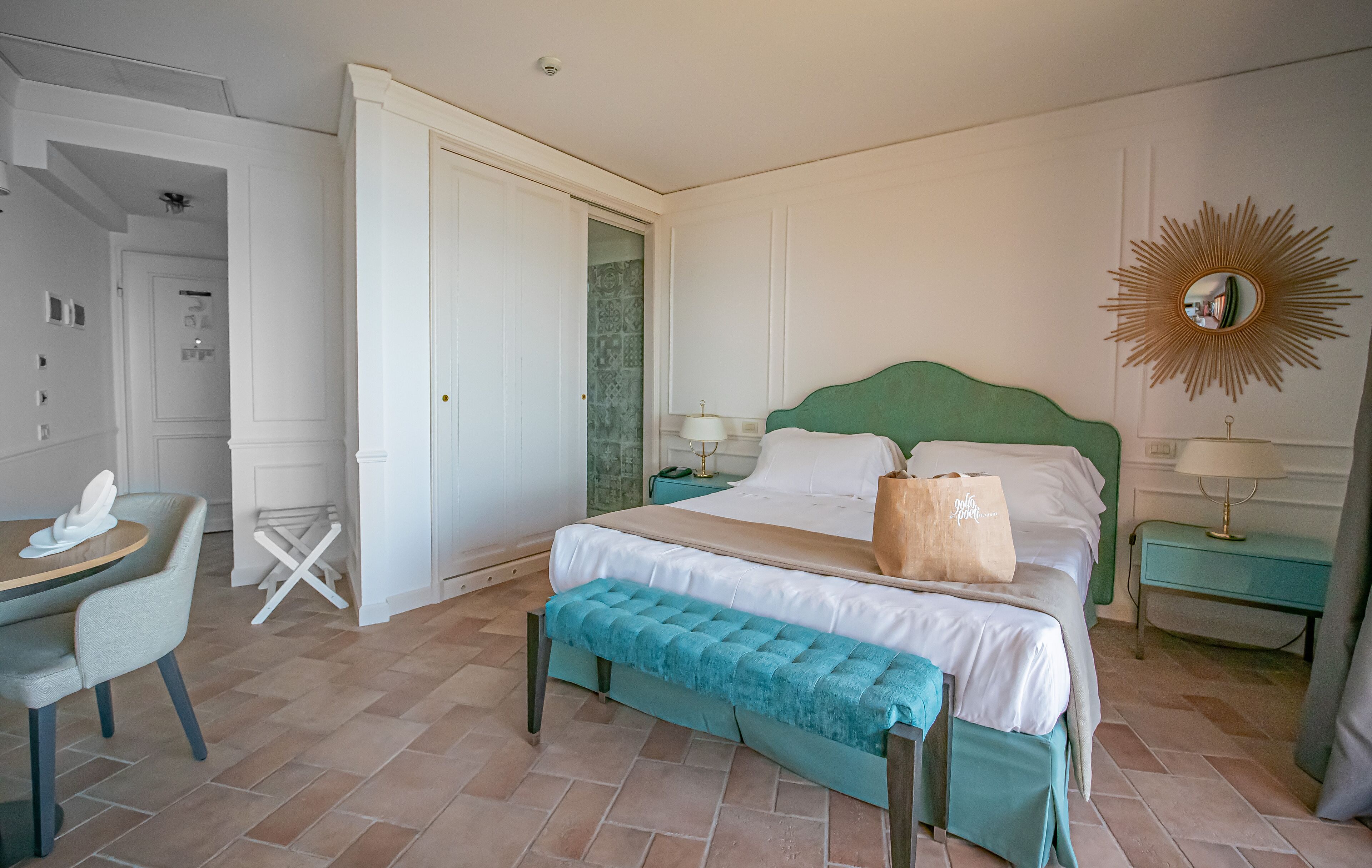 A neatly arranged bedroom with a bed, bedside tables, a bench, a chair, and a door leading to another room.