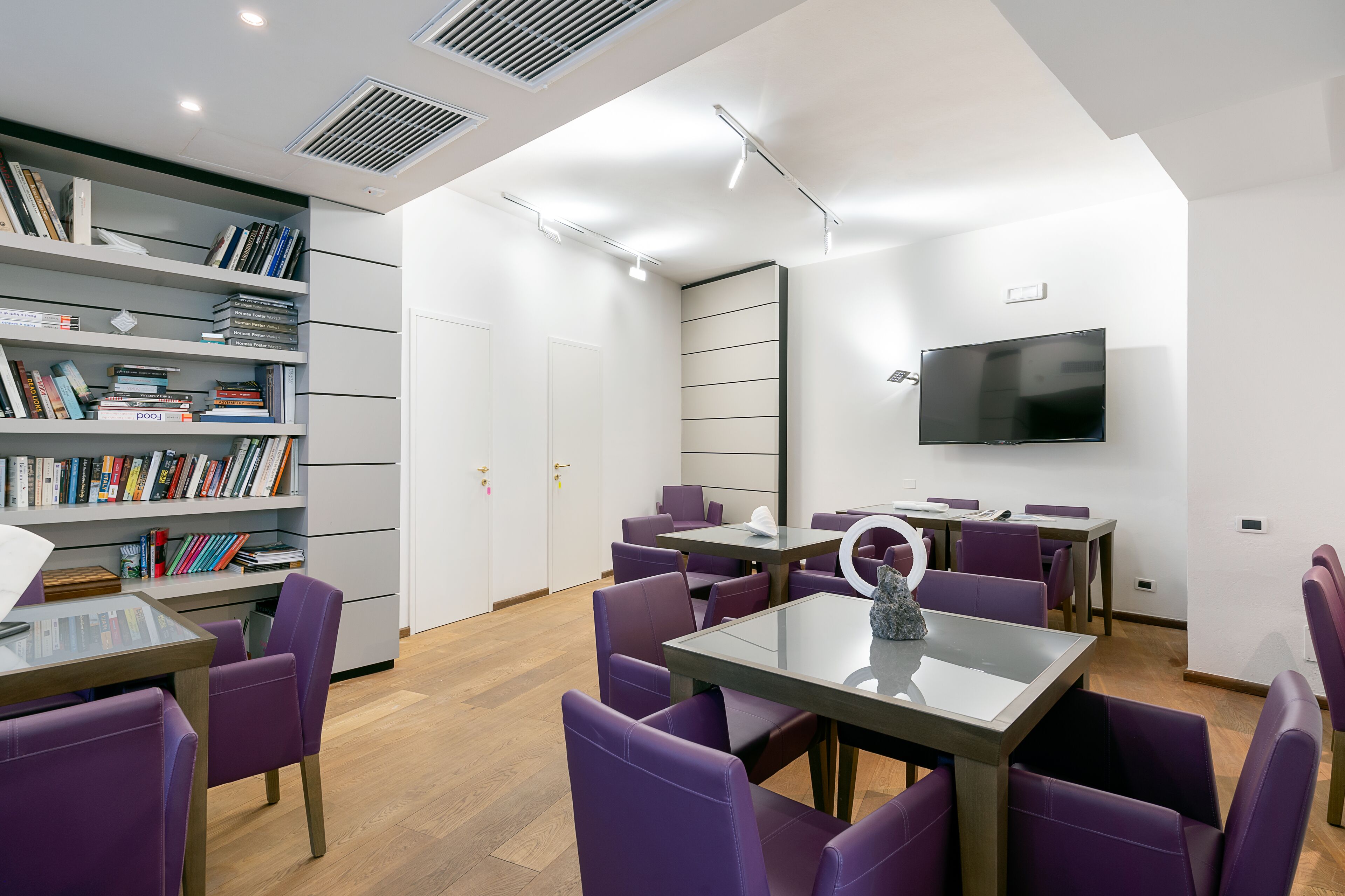 Una sala de reuniones moderna con sillas y mesas moradas, una estantería y un televisor de pantalla plana en la pared.