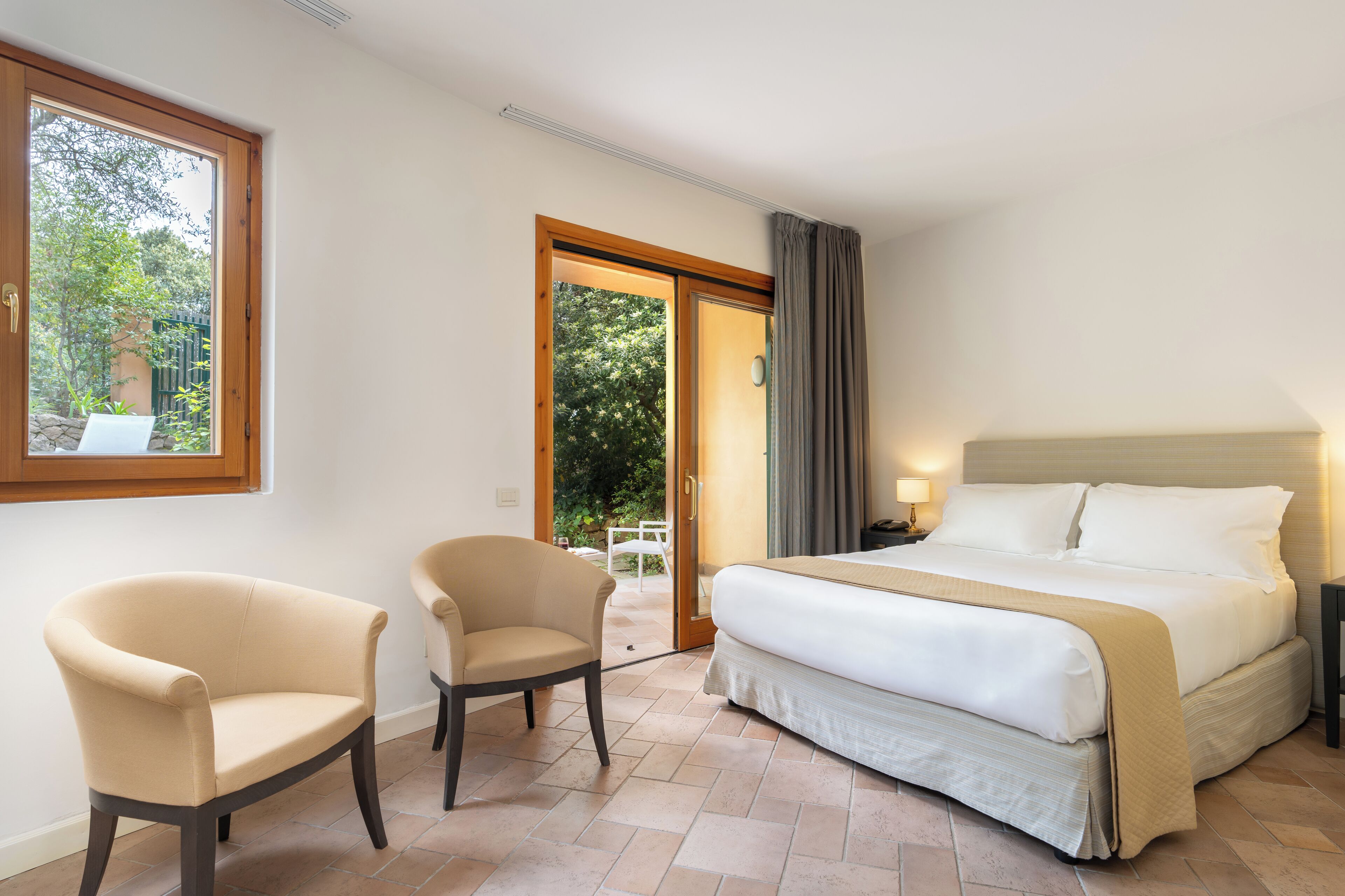 A hotel room with a bed, two armchairs, a window, and a door leading to an outdoor area.
