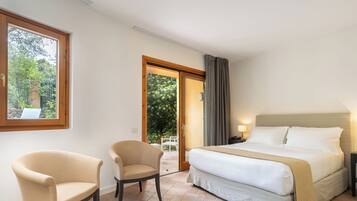 A hotel room with a bed, two armchairs, a window, and a door leading to an outdoor area.