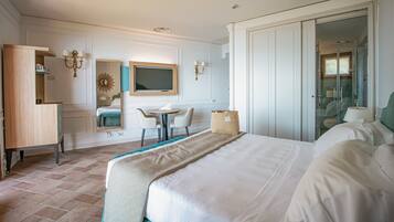 A hotel room with a bed, a desk, a chair, a small table, a mirror, and a wardrobe.