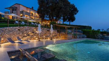Área de piscina com espreguiçadeiras, guarda-sóis e um muro de pedra.