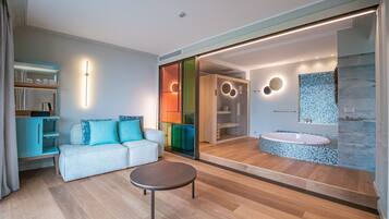 Una habitación de hotel moderna con sofá, una mesita, baño con bañera y un espejo grande.