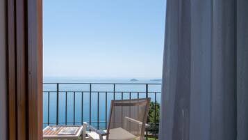 Un balcone con una sedia e un tavolo, vista su un mare azzurro e una costa lontana.