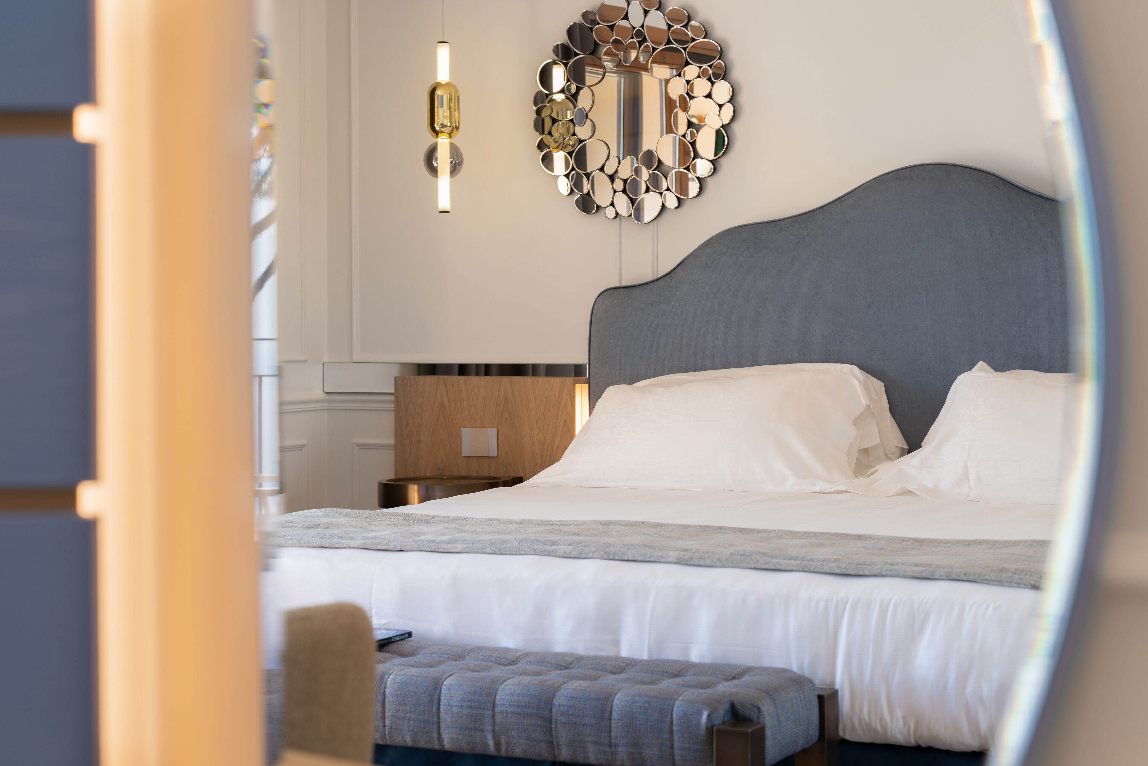 A bedroom with a large bed, a bedside table, a mirror, and a hanging light fixture.