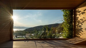Quarto com uma grande janela com vista panorâmica para colinas e um corpo d'água.