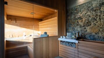A sauna with wooden benches, a stone wall, and a small table with towels and toiletries.