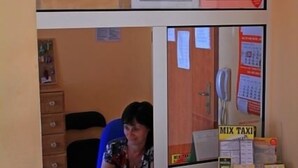 A reception area with a sign reading "RECEPCJA" above a counter. There are papers on the wall, a phone, and a "MIX TAXI" box on the counter.