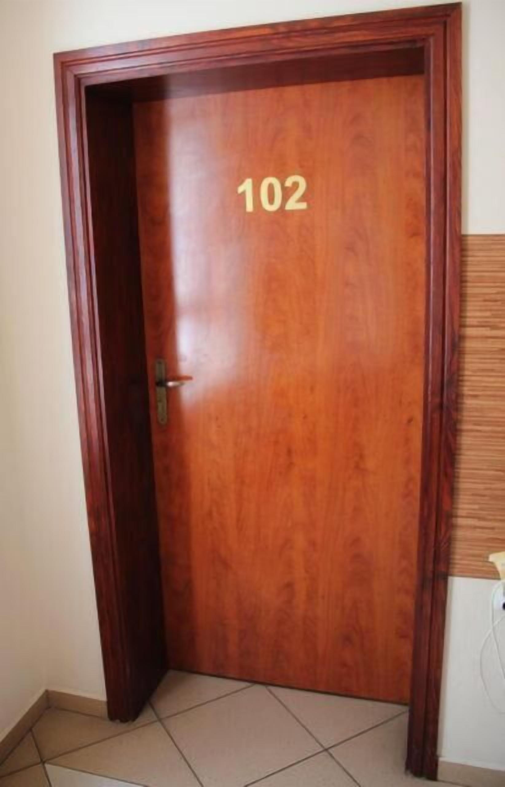 A wooden door with the number 102, a metal handle, and a partial view of a tiled floor.