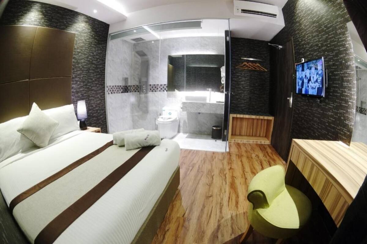 A modern hotel room with a bed, a shower, a vanity, and a television.