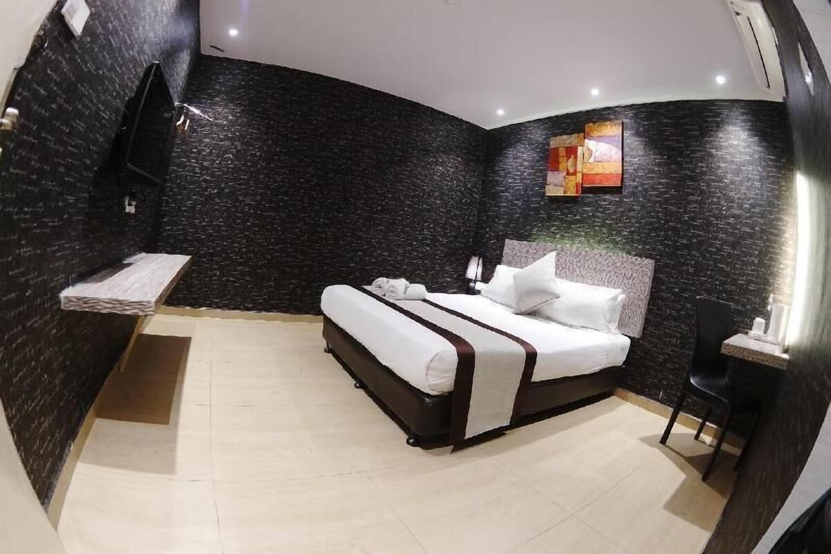 A hotel room with a bed, a small table, a chair, and a wall-mounted TV.
