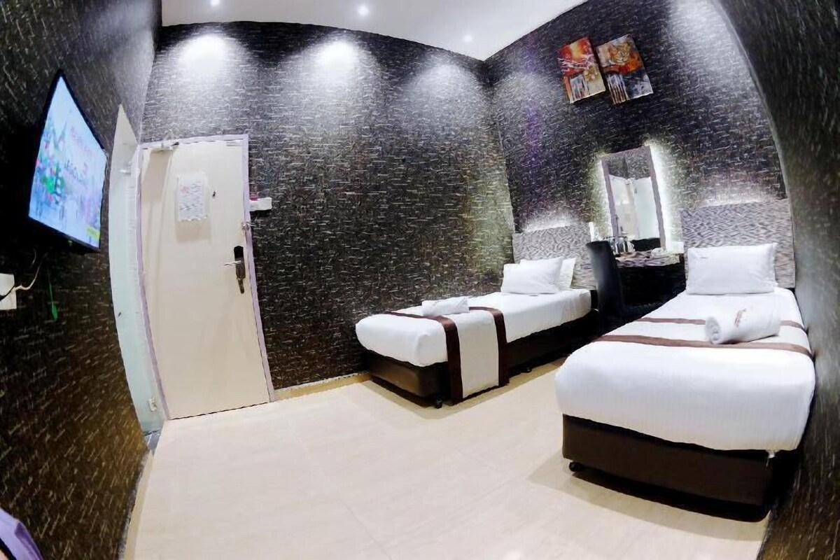 A hotel room with a dark textured wall, a flat-screen TV, two beds, a mirror, and a door.