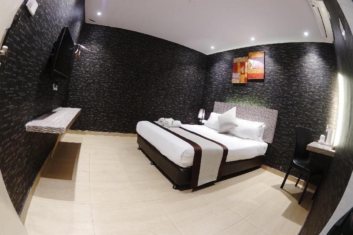 A hotel room with a bed, a small table, a chair, and a wall-mounted TV.