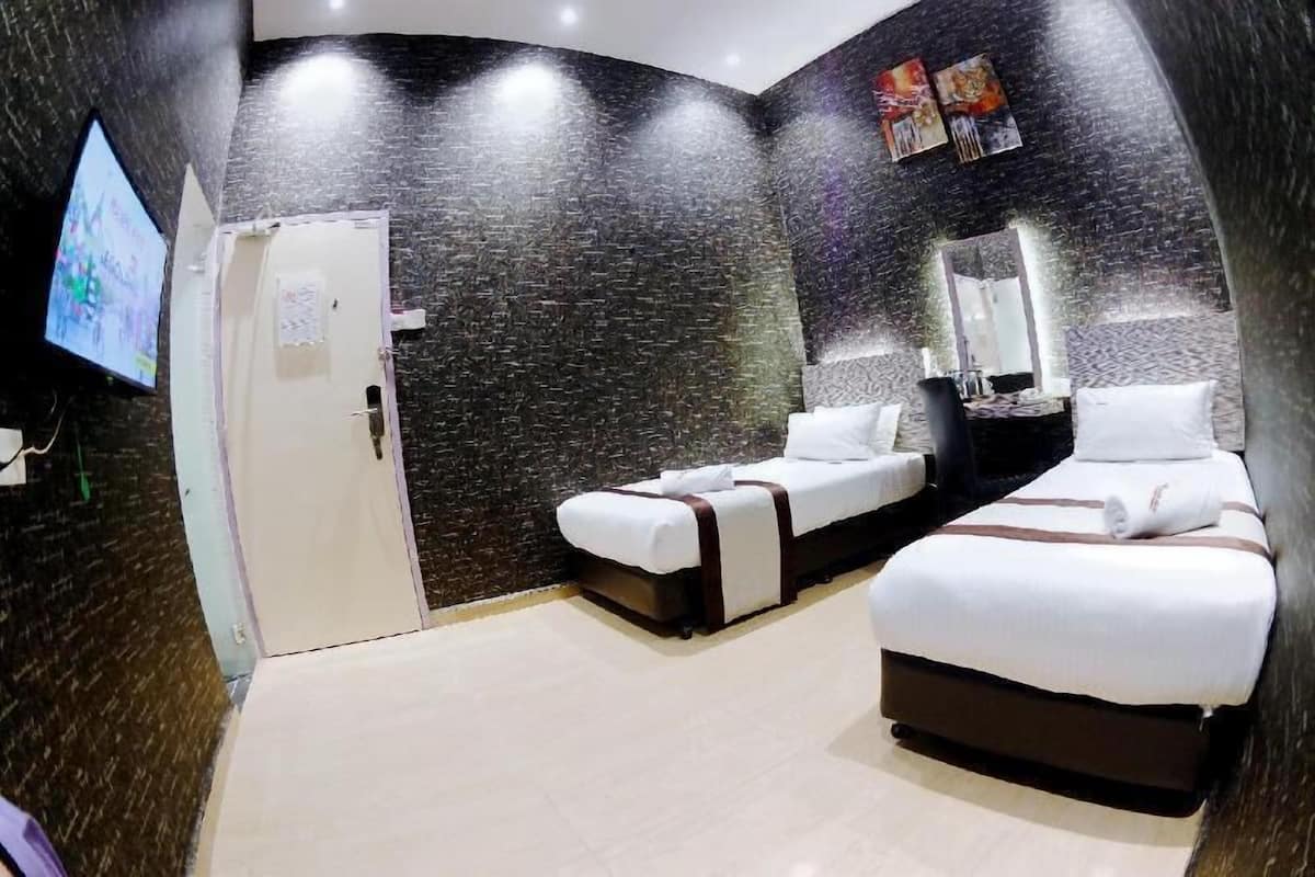 A hotel room with a dark textured wall, a flat-screen TV, two beds, a mirror, and a door.