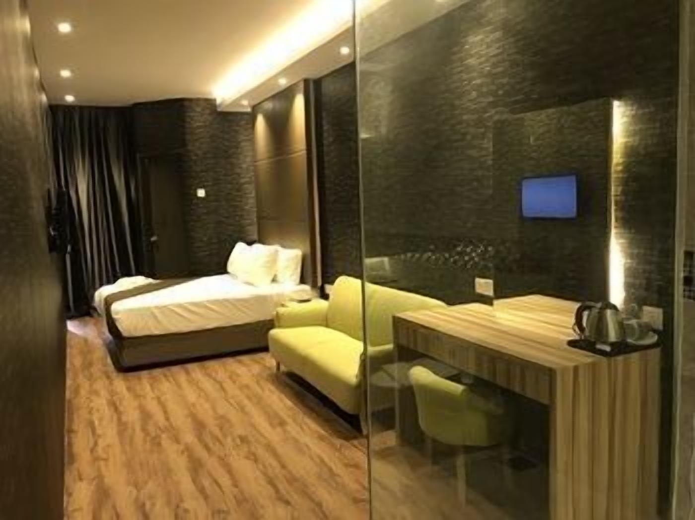 A modern hotel room with a bed, a seating area, a desk, and a television.