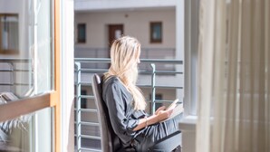 A person sitting on a chair by a window with a view of a building. - Prince Apartments (Budapest)