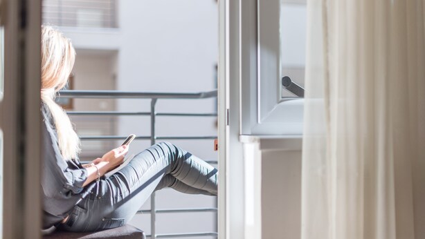 A person sitting by a window, using a smartphone. - Prince Apartments (Budapest)