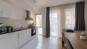 A modern kitchen with white cabinets, a black countertop, and a dining area with a wooden table and chairs. - Prince Apartments (Budapest)