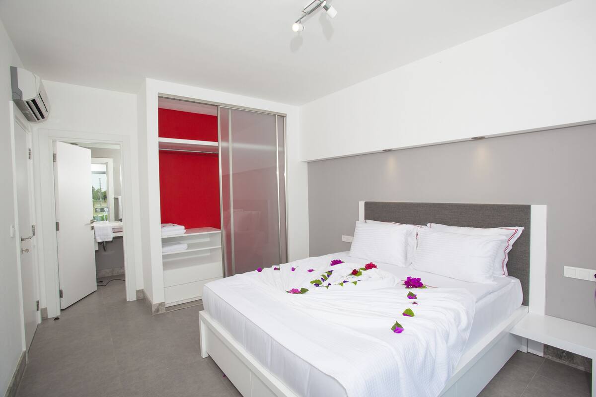 Quarto de hotel moderno com uma cama grande, um closet espaçoso e uma parede de destaque vermelha vibrante.